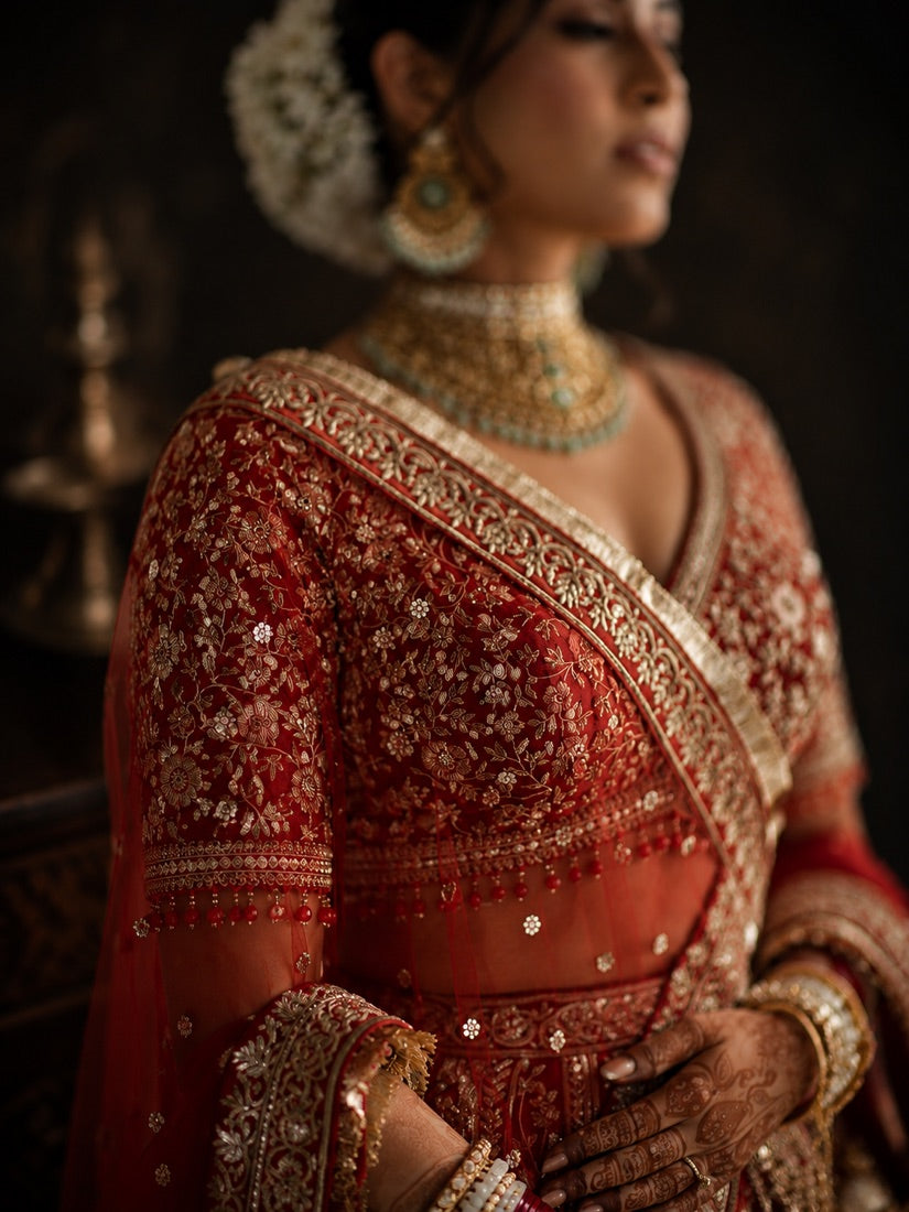 A bride in a red-and-gold bridal lehenga with kundan jewellery and gajra, dressed by Label Neha Sinha